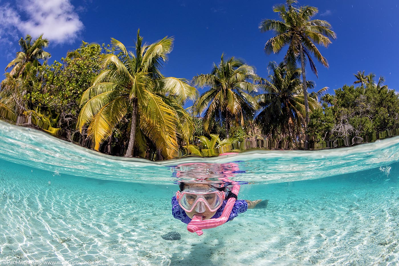50. Over-under view of child (female) snorkelling in shallow water lagoon, Fakarava, Tahiti